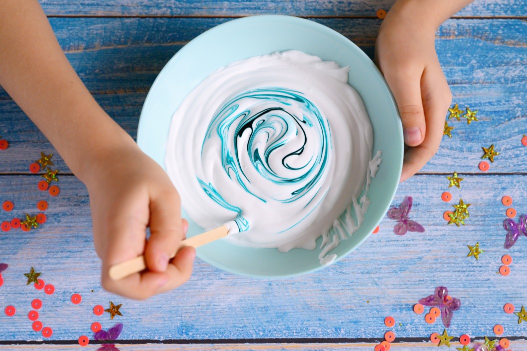 a-little-girl-hands-making-slime-herself-on-blue-wooden-background