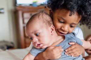 Toddler holding his baby sibling.