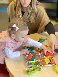 Mom helping preschooler do a puzzle at a table.