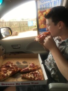 Kid eating pizza in the car.