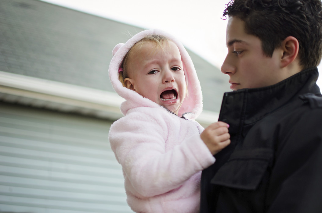 Toddler crying in siblings arm.