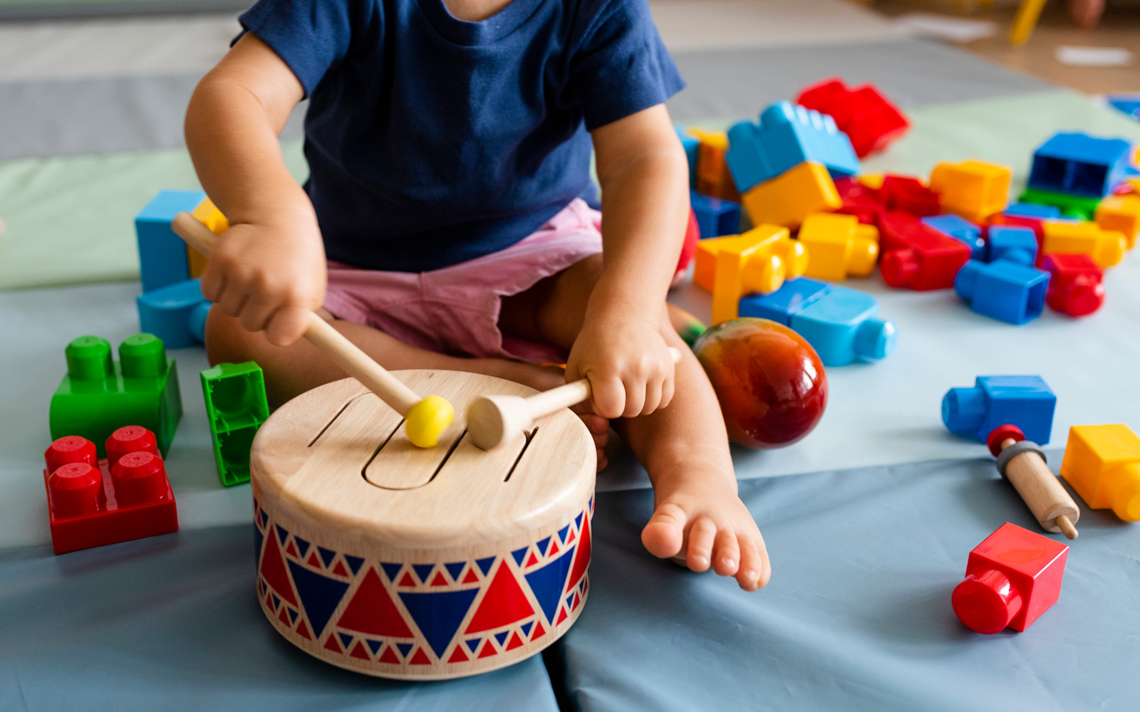 Toddler playing toy drum surrounded by blocks
