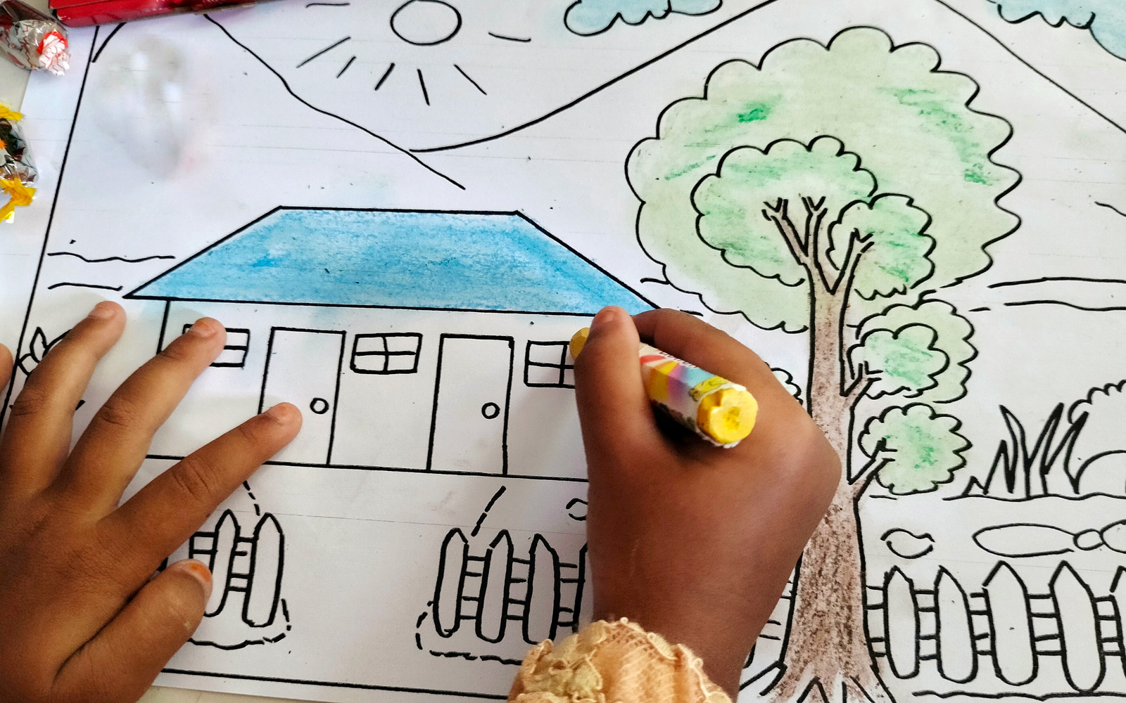 Child coloring a house and tree scene